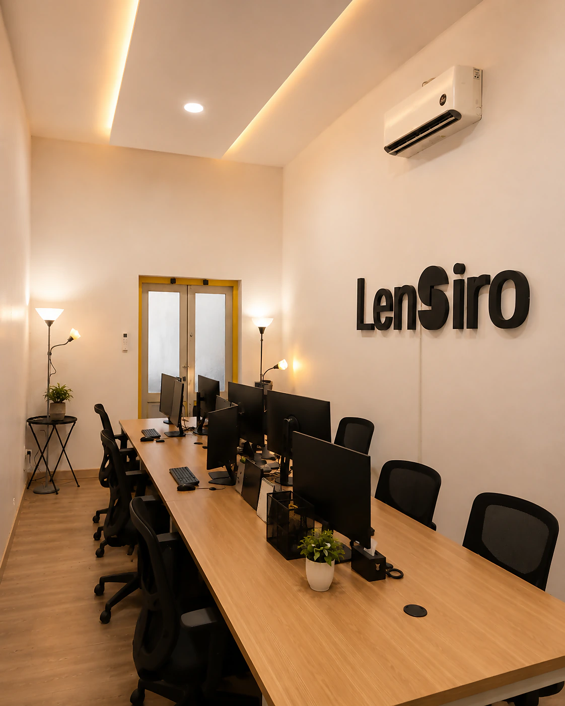 Ruang kerja PT Lensiro Digital Solusi di Lumajang: satu meja panjang, deretan monitor, dan tulisan Lensiro di dinding